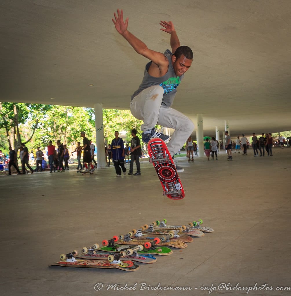 Skateboarder shown in mid-flight attempting a trick where we leaps over 7 skateboards laid out horizontally.